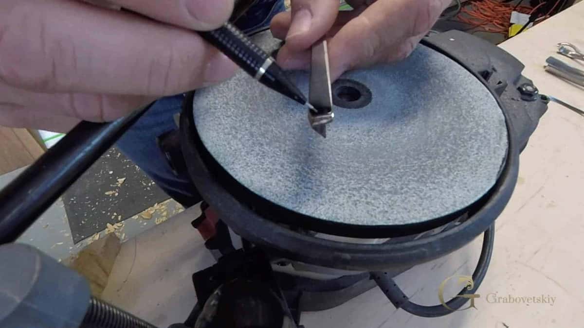 A marker and a V-tool over the grey stone of a bench grinder, wheel guard above