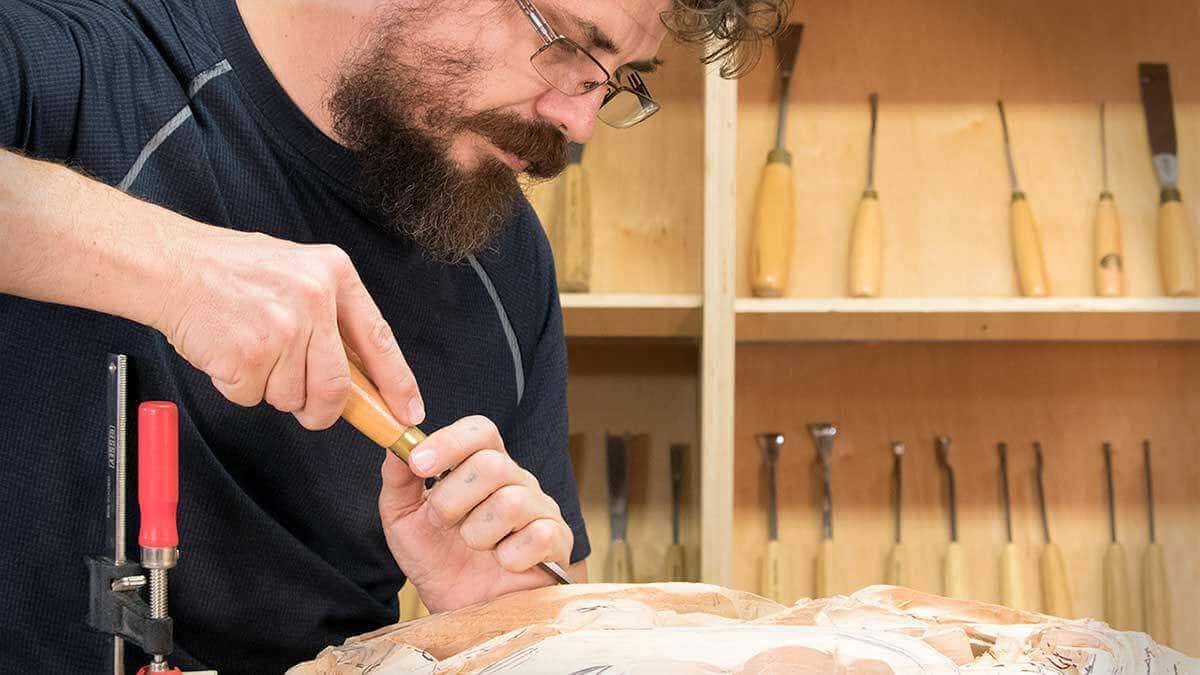 Carving a panel below racked rows of chisels