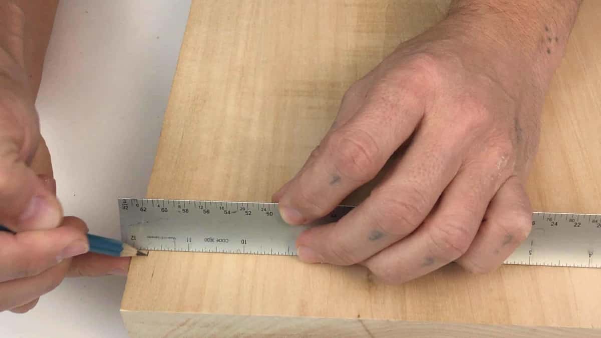 Steel rule laid along a bare board while a blue pencil squares the first line off its edge