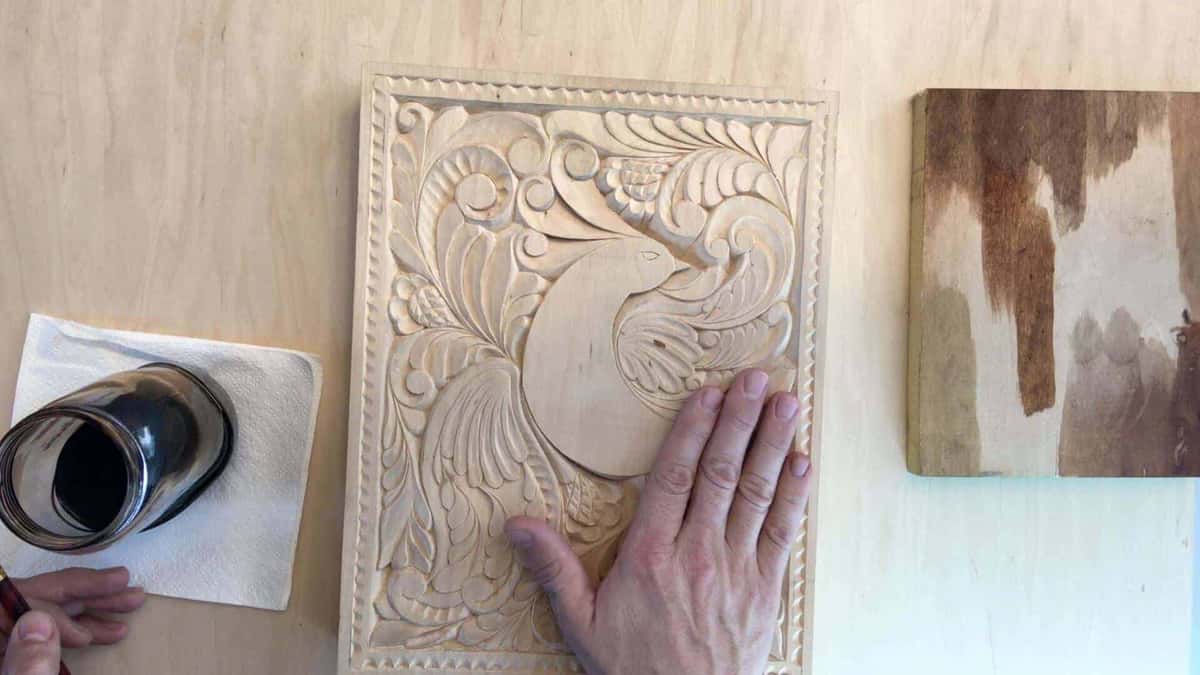 A finished floral panel beside a small scrap board brushed with several different test patches of stain