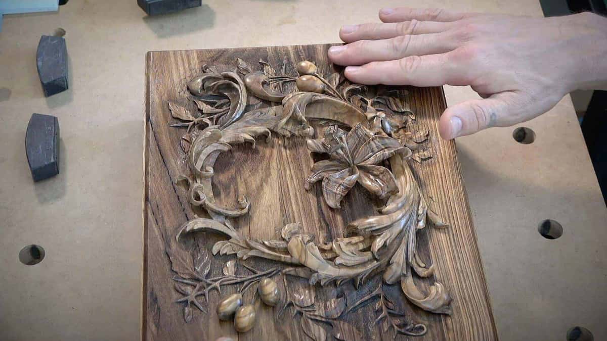 Lily and leaves finished in pale figured olive, standing off a dark board with a hand resting flat