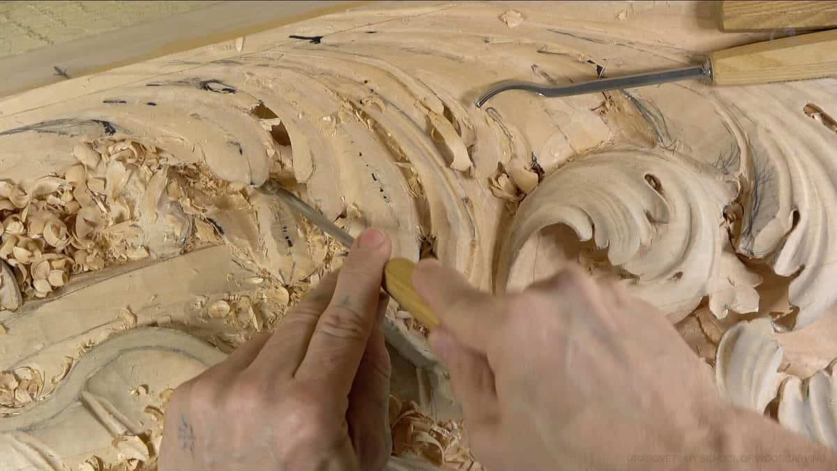 Hands with a small gouge on a broad acanthus scroll panel, long shavings banked to the left.