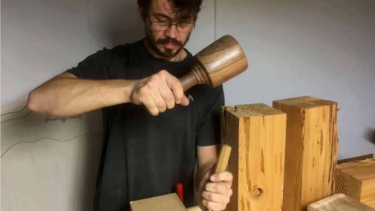 Alexander Grabovetskiy swings a large turned wood mallet over blocks of knotty orange softwood, a gouge in his left hand