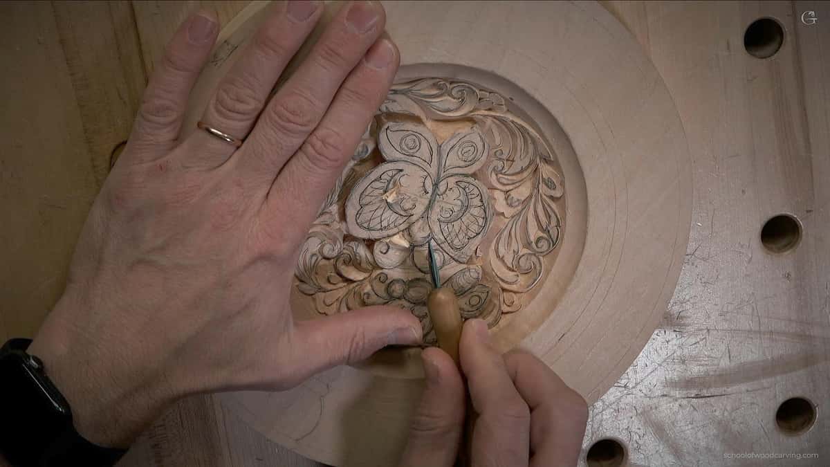 One hand steadies the round plate while the other guides a small knife along the pencil lines
