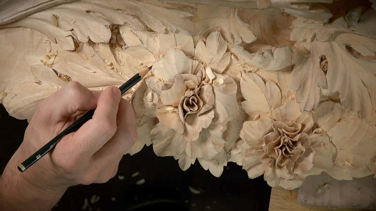 A close-up of a skilled hand carving detailed floral designs into a piece of wood, showcasing beautiful roses and leaves. This image highlights the intricate work involved in wood carving and is perfect for wood carving classes and lessons. Perfect for those wanting to learn the art of wood carving!