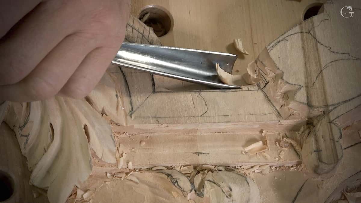 A gouge lifts one curl of wood from the pencil layout, the design still only lines on a flat board