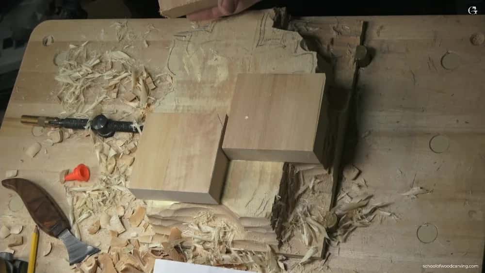 Three plain square blocks of pale wood resting on a shaving covered bench, a carving knife and glue nozzle nearby
