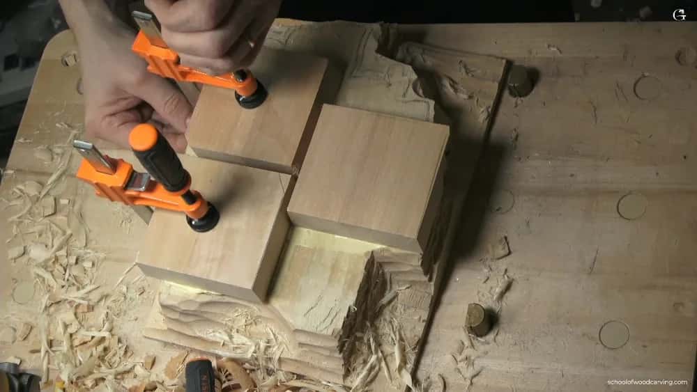 Two orange spring clamps holding fresh blocks down on a carving while the glue takes hold