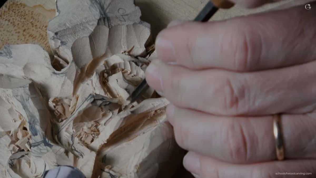A grape cluster and leaf roughed out under pencil lines, a fine chisel held in a hand wearing a plain gold ring.