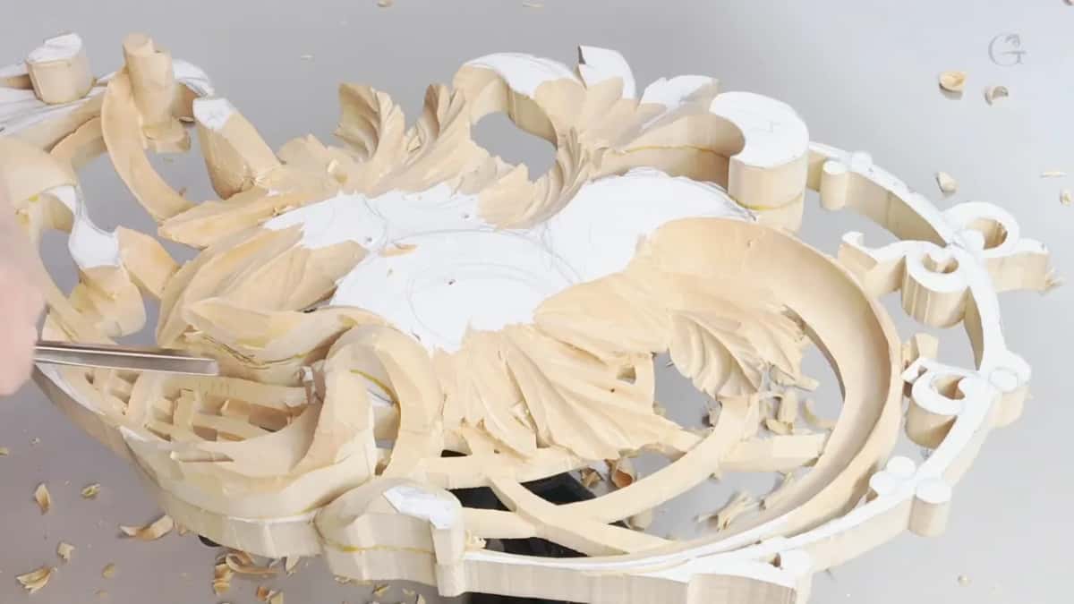A big oval frame pierced right through, acanthus leaves standing free of the ground, white primer marks between them.