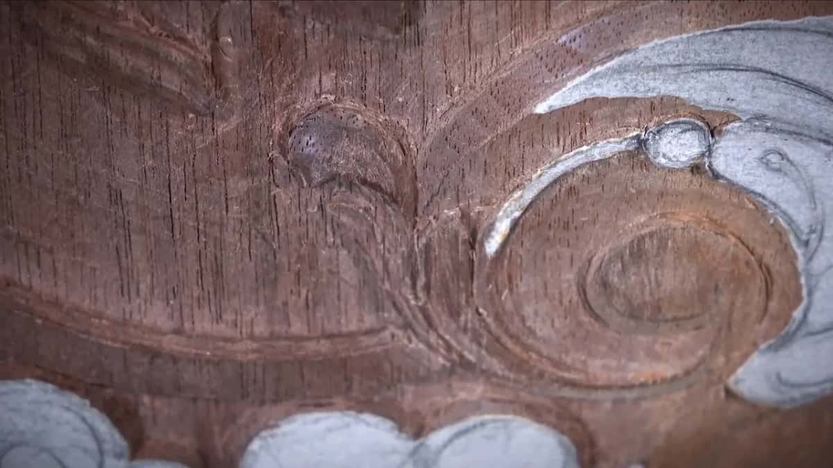 Soft-lit macro of reddish-brown relief carving: a small bud and a rolled scroll, no hands in the frame.
