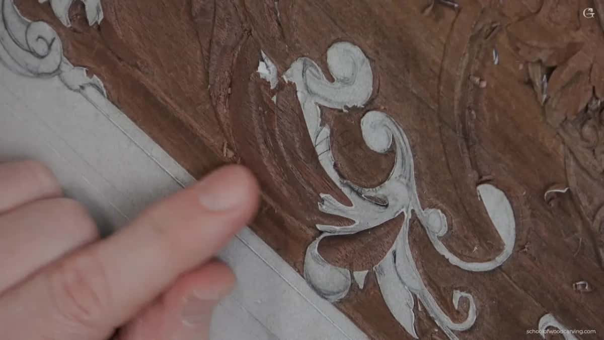 A pale grey drawing of an acanthus sits above the lowered ground of a reddish-brown panel, fingertip at left.