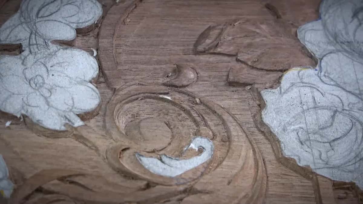 Macro of a reddish-brown carved scroll eye showing tool facets, with pale drawn petals on either side.