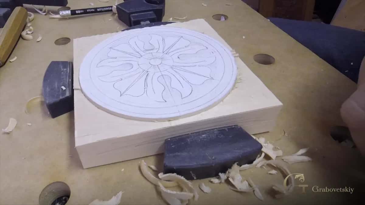 A pale close grained block carries a rosette drawn in pencil, and long curled shavings lie all around it.