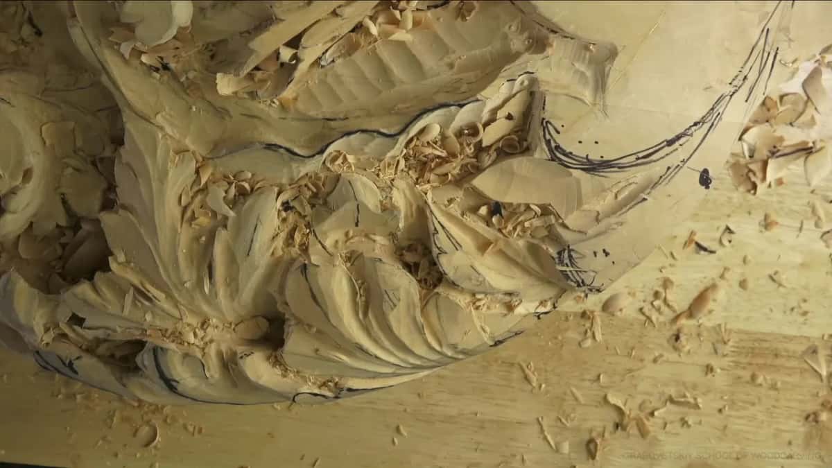 Deep acanthus leaves roughed out of pale wood, ink layout lines and chips still on the surface.