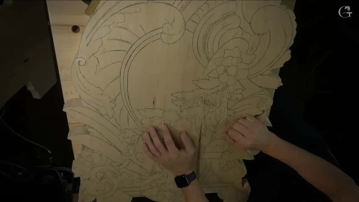 Hands hold up a wide pale panel with the whole design drawn in pencil and a joint line down the middle.