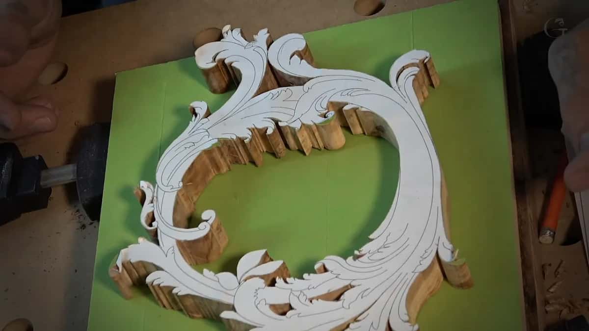 An olive wood scroll blank sawn out on the bandsaw, paper pattern still glued to its face, on a green mat.