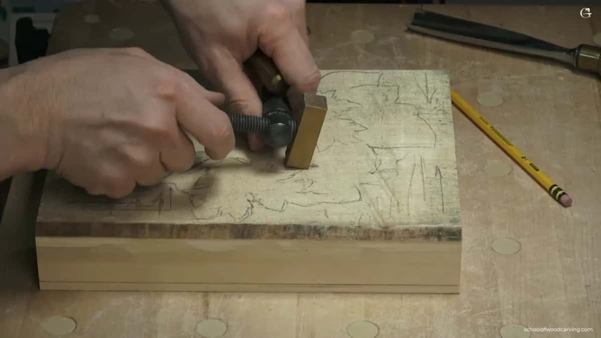 Two hands setting a brass screw clamp against a thick block, the top carrying a penciled design and grain arrows