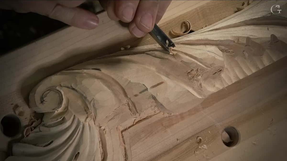 One curl of shaving lifts off a carved scroll under the gouge, low light raking across the marks.