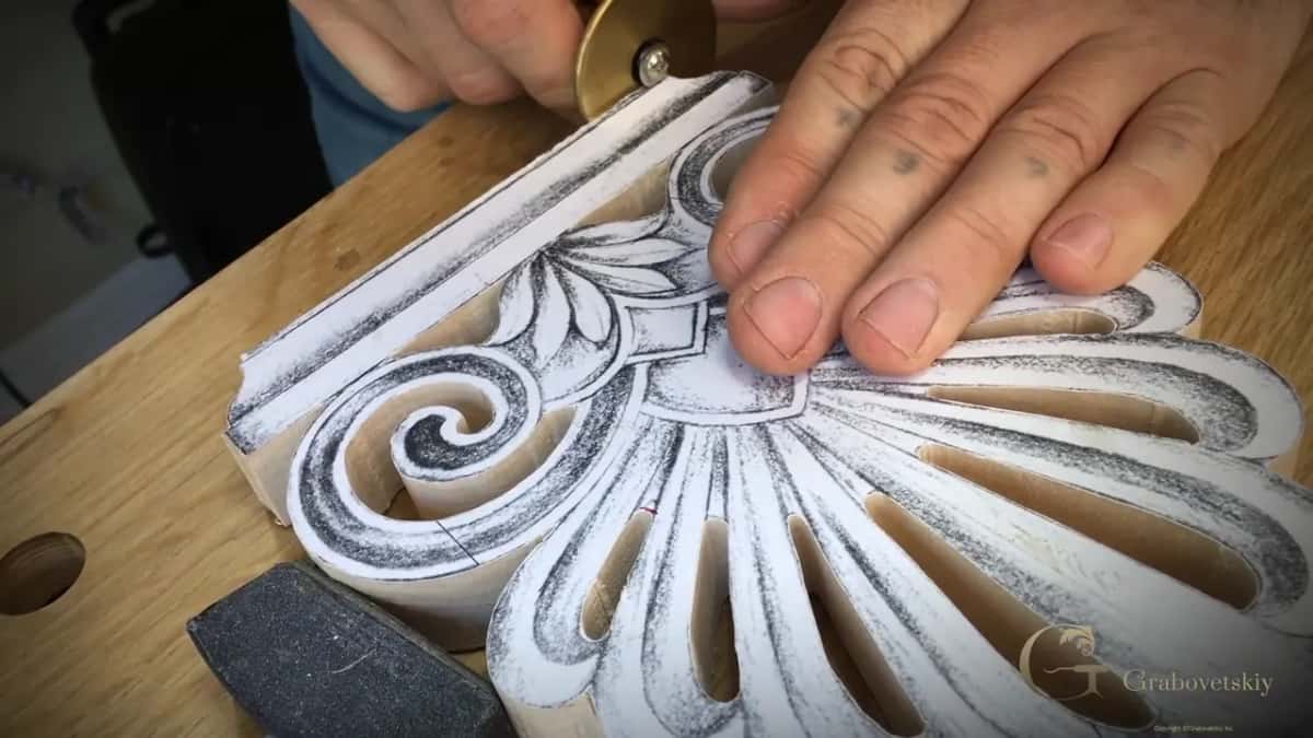 A paper pattern glued to a sawn block, its fan of petals already pierced through, one hand pressing it flat.