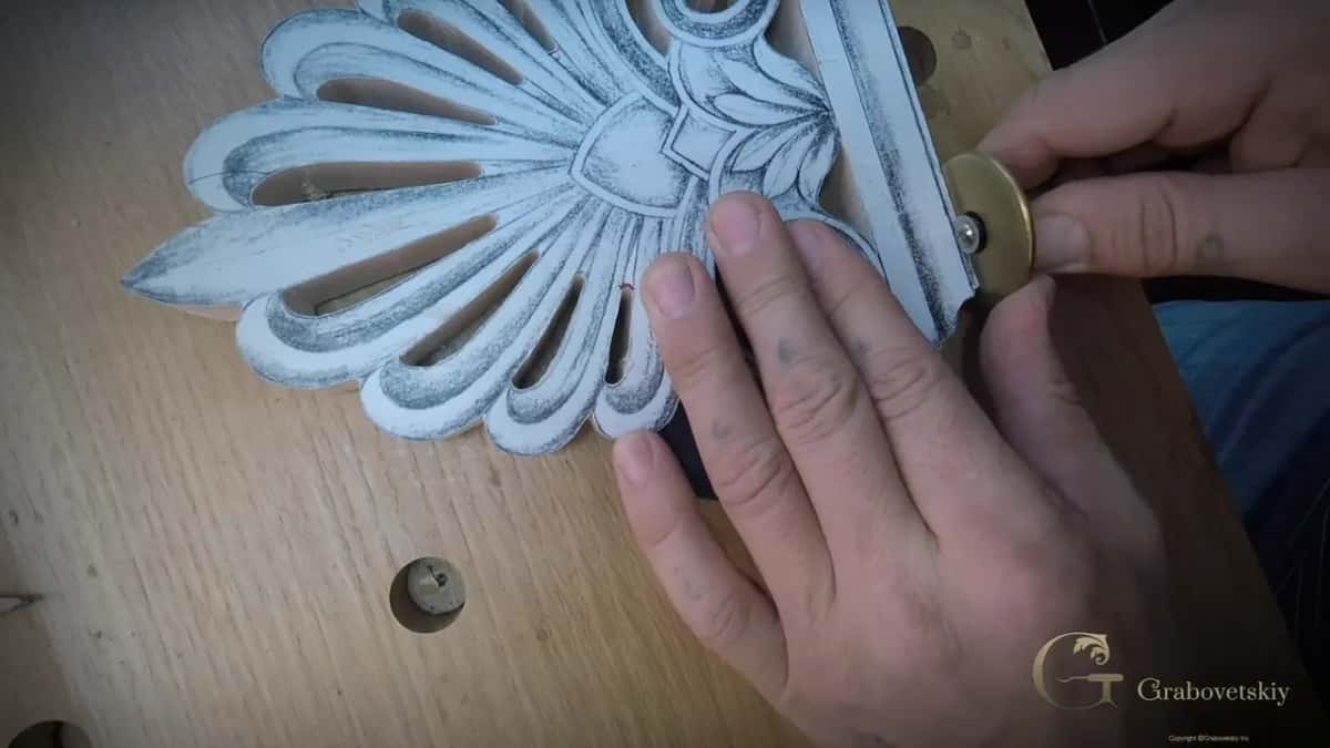 The pierced block from above, one hand spread over the paper pattern, the other steadying a brass collared tool.