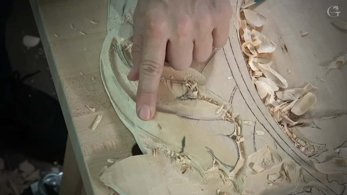 A finger rests on one pencil line across a half carved panel, fresh chips gathered in the hollow beside it.