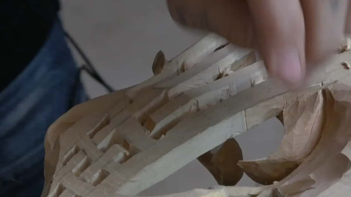 Fingers rest on a carving where the bands of wood have been carved down to narrow standing ribbons.