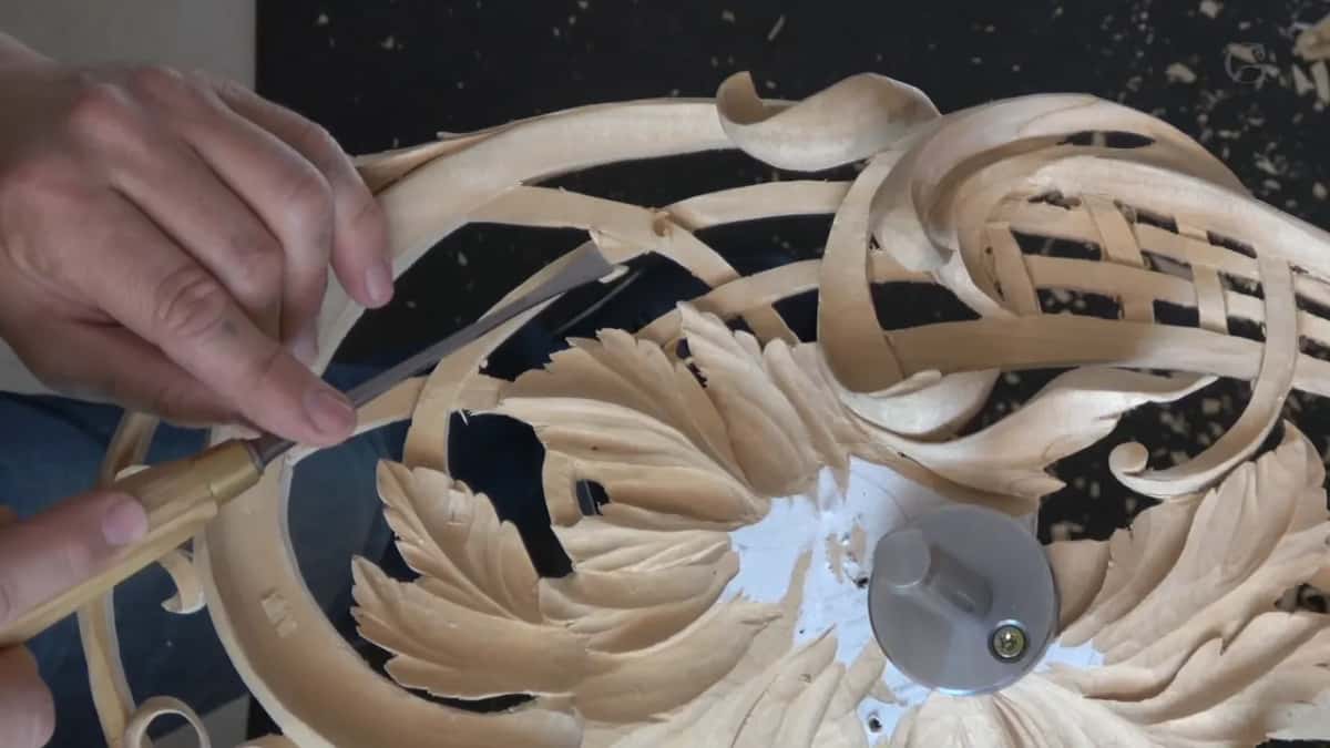 Seen from above, a pierced round panel shows black openings between its carved ribbons and leaves.