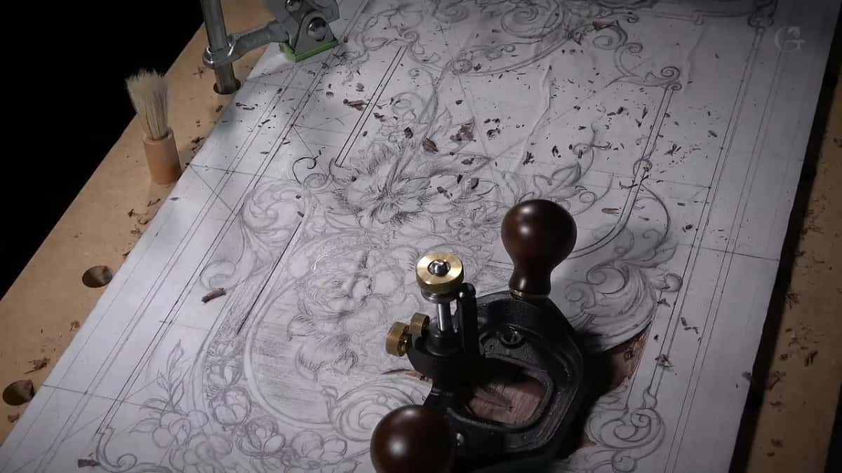 A small cast iron plane with two round handles rests on a paper drawing laid over a dark board.