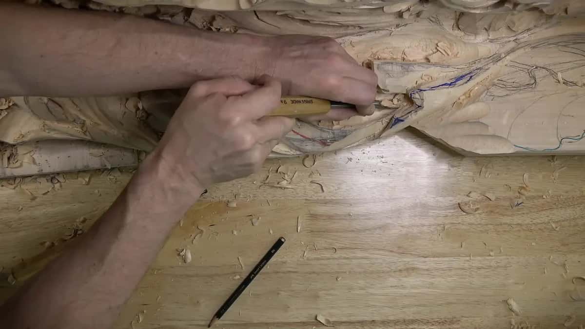 Both hands guide a small blade along the roughed out panel, one pushing and one holding it steady.