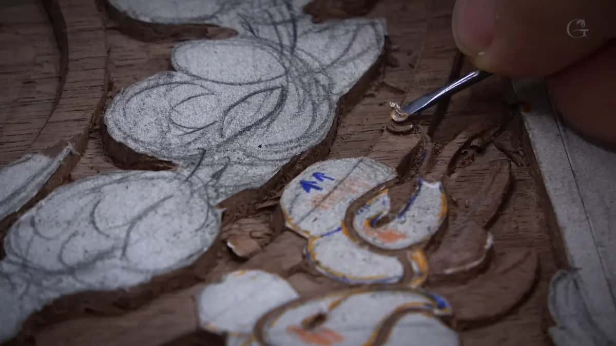 A small tool lifts a chip the size of a rice grain from a brown board drawn on in chalk and pencil.
