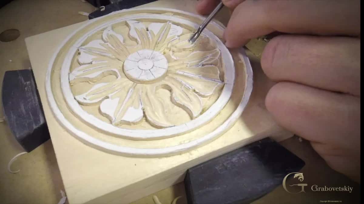 A finished pale rosette of twelve petals sits in its sunk ring, a fine tool touching one petal tip.