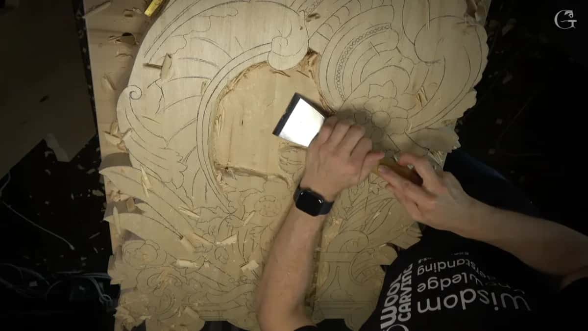A wide flat chisel is pushed across a large pale panel whose whole design is drawn on in pencil.