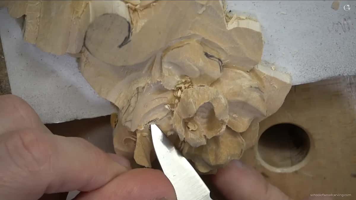 A knife blade cuts in at the base of a pale carved rose to free the petals from each other.