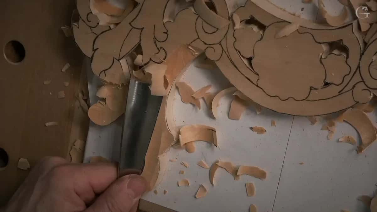A wide gouge slices the edge of a sawn pale ornament, thick curls of wood scattered over the paper.
