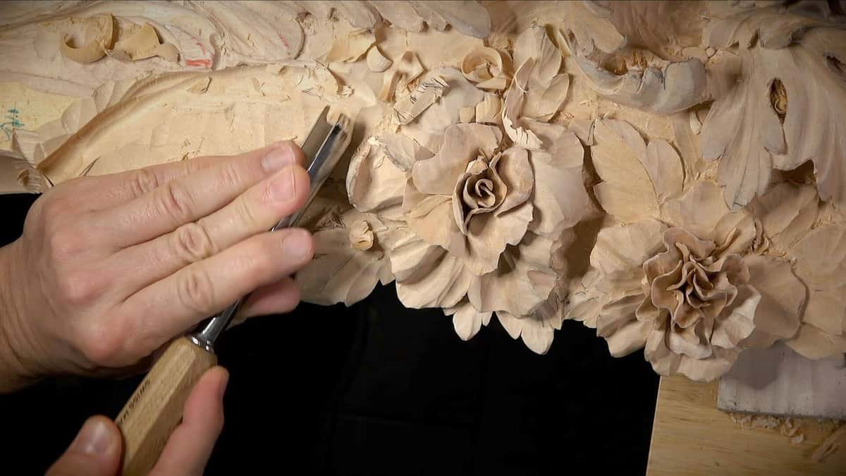 A gouge resting on a leaf beside finished roses, with a fuzzy torn edge on the wood to the left.