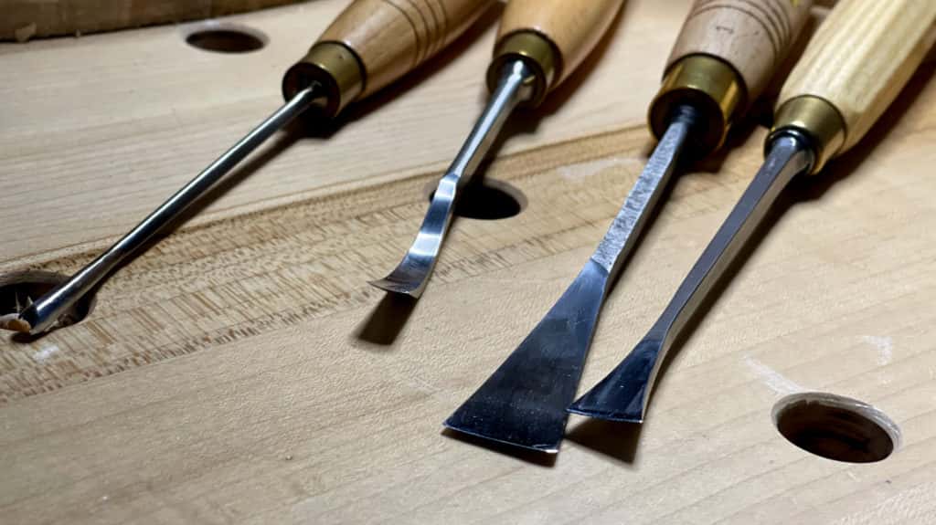Basic wood carving tools with wood handles laid out on a workbench