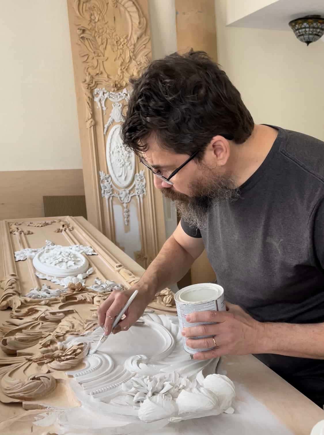 White primer goes into the hollows of a carved panel, a tall finished door standing behind