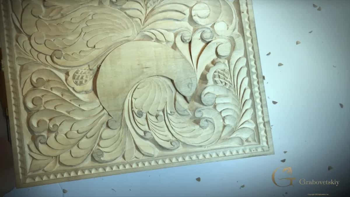 A square pale panel finished with deep leaf scrolls and a beaded border, chips still in the air.