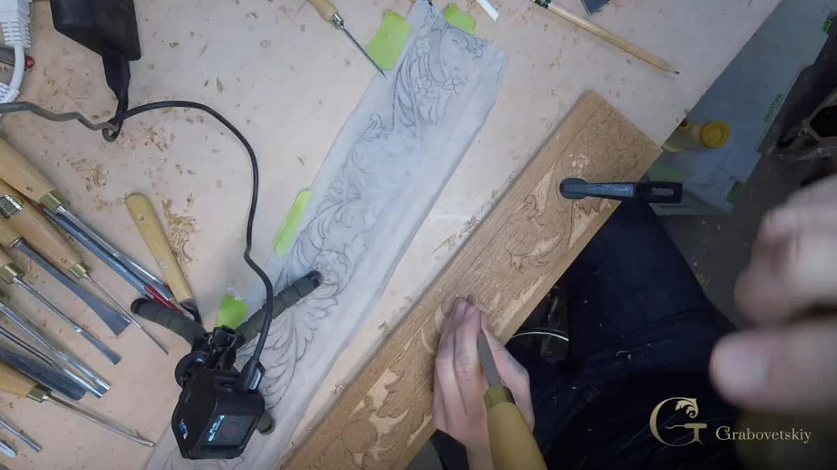 Overhead view of a bench: a row of gouges, a paper drawing, and a long tan board part carved.