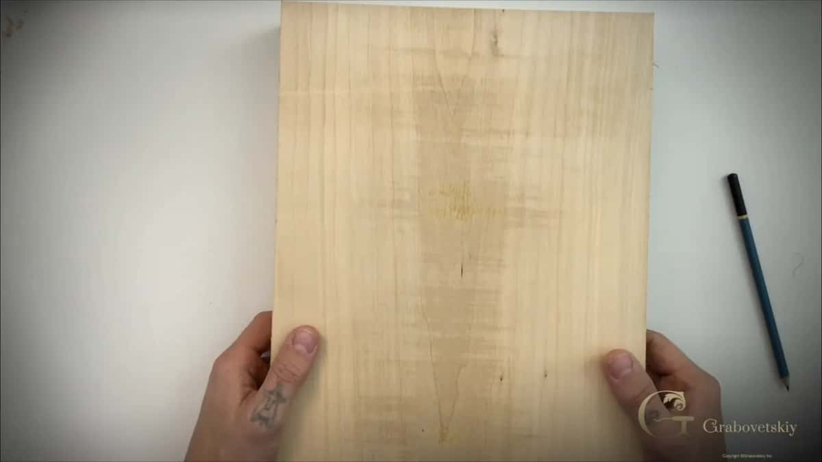 Two hands hold a pale plank upright against a white wall.