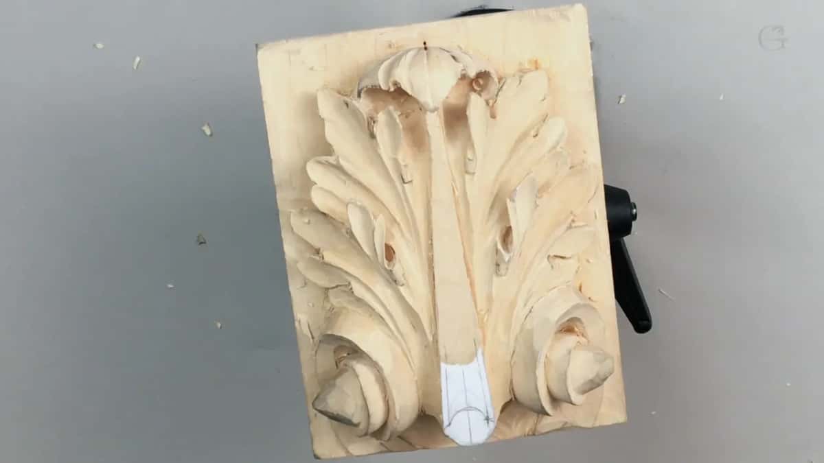 A small pale board carved with one acanthus leaf, photographed from above on a plain grey surface.