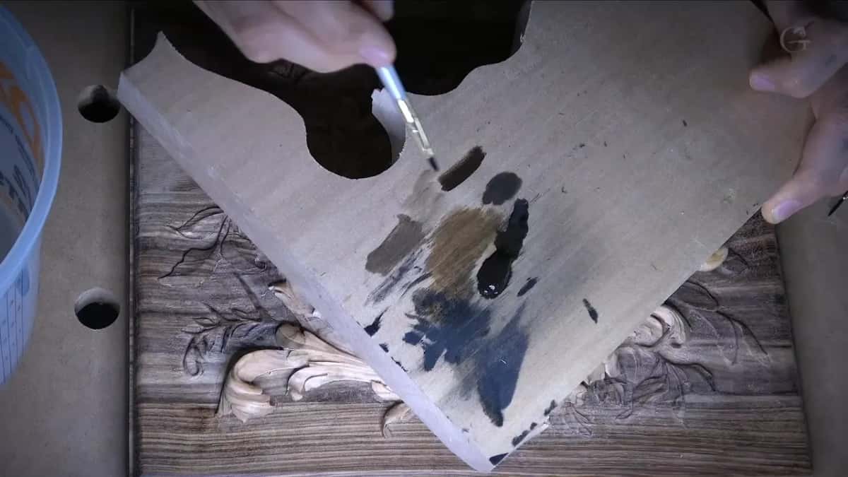 Black, brown and grey stain swatches brushed onto a pale scrap board held over a finished carving.