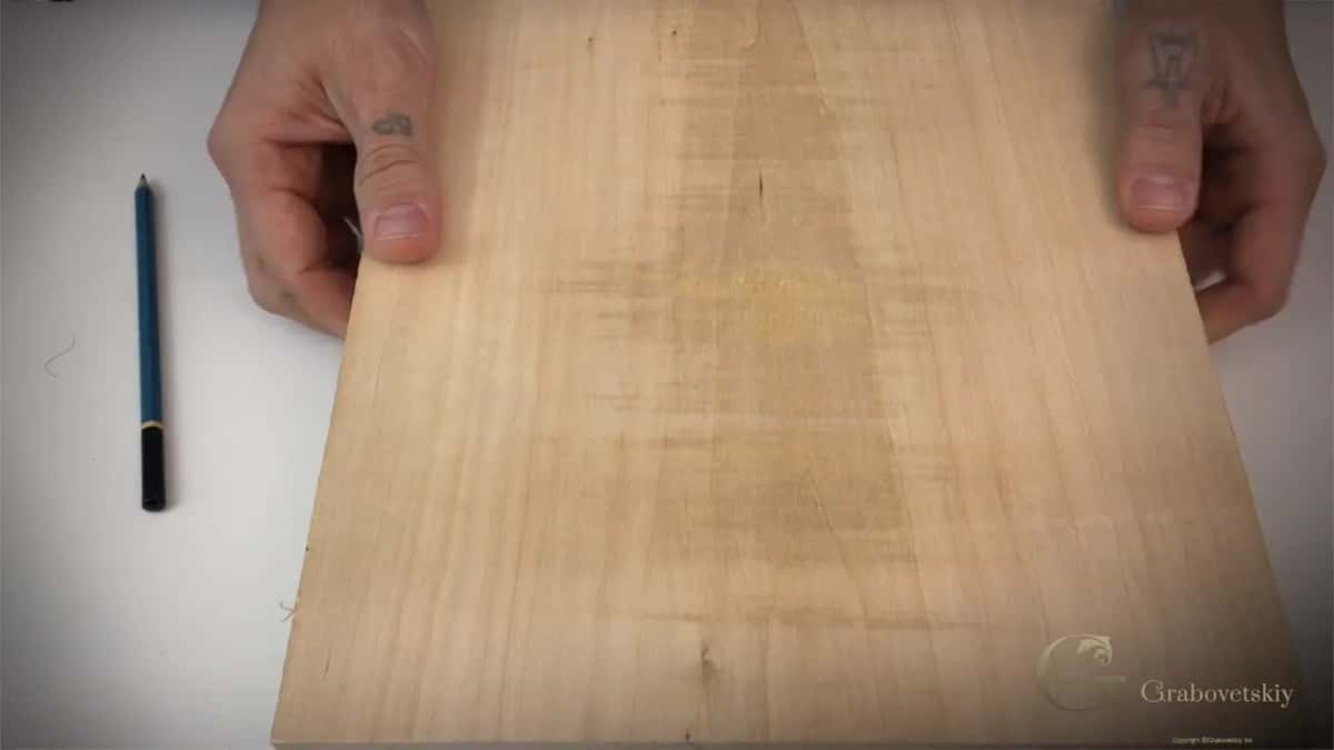 Bare basswood board held flat on the bench with a pencil beside it, before any line is drawn