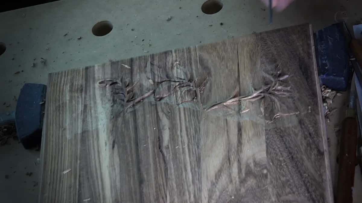 A dark board clamped to the bench with three small sprigs carved in shallow relief across the middle.