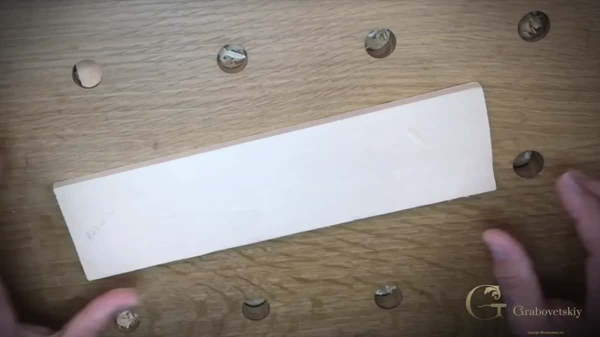 A dried basswood plank ready to carve A dried basswood plank flat on a dog hole bench with two hands holding the far edge steady, the beginner wood carving setup