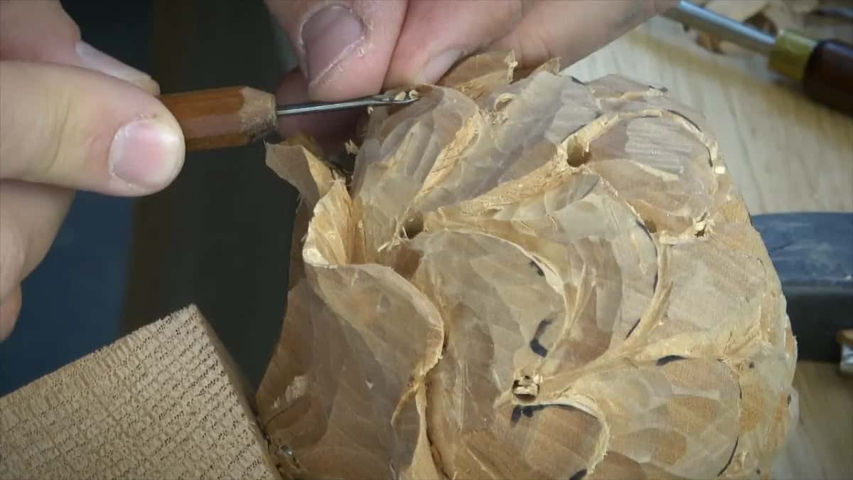 A small palm tool shapes a partly carved pale rosette, pencil lines still on the petals.