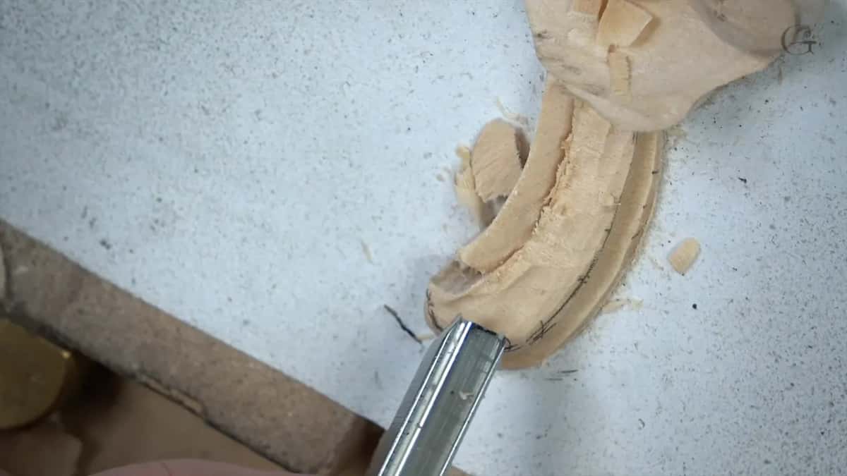Close view of a gouge blade running along a raised leaf, the freshly carved surface still rough and hairy.