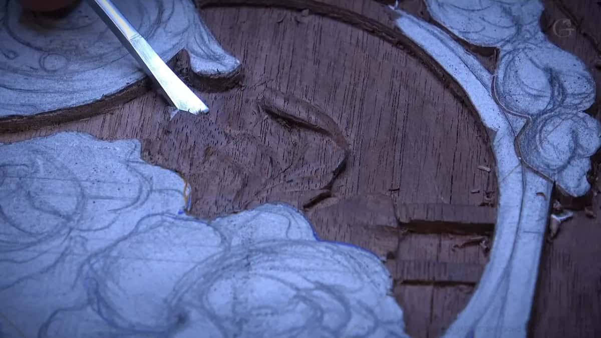 A bright chisel blade angled into the lowered background of a dark open-grained panel.