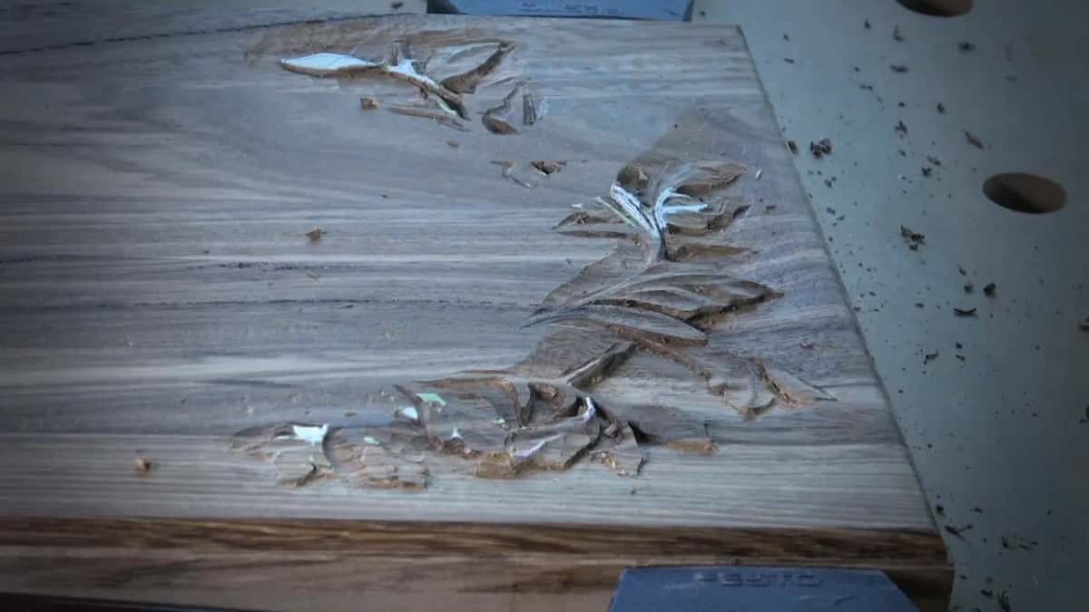 A dark streaked board with a floral design roughed out, white layout paint still sitting in the hollows.